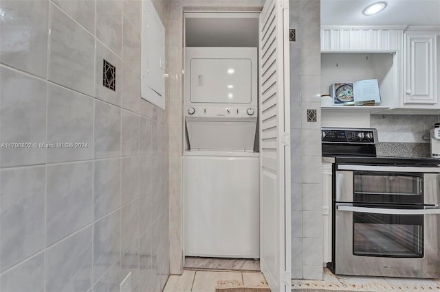 kitchen with stainless steel electric range, stacked washer and dryer, light tile patterned floors, tile walls, and white cabinetry