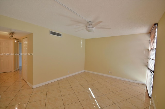 empty room with a textured ceiling, ceiling fan, and light tile patterned flooring