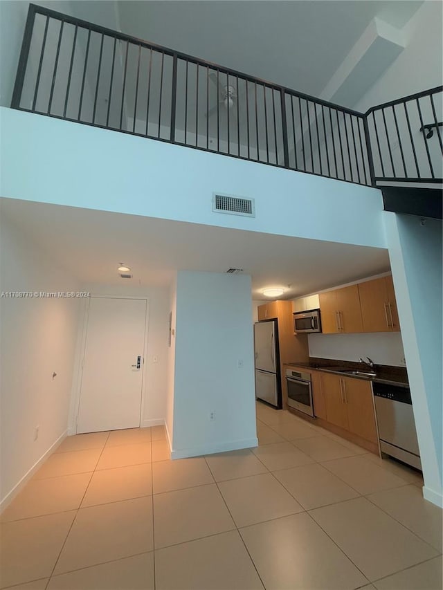 kitchen with light tile patterned floors, a towering ceiling, sink, and appliances with stainless steel finishes