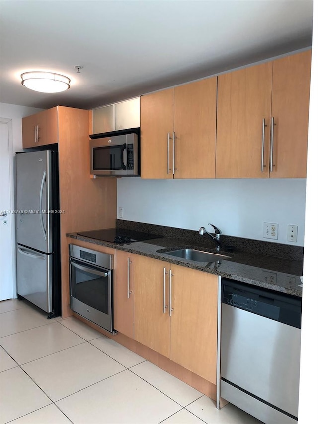 kitchen with dark stone counters, sink, light tile patterned floors, and stainless steel appliances