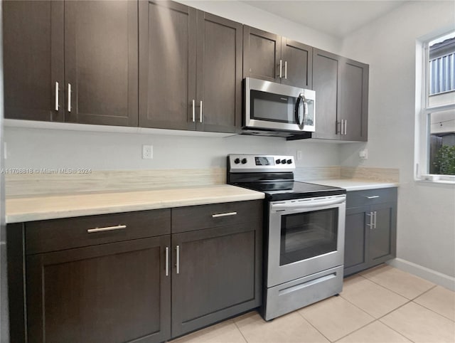 kitchen featuring dark brown cabinetry, light tile patterned flooring, and appliances with stainless steel finishes