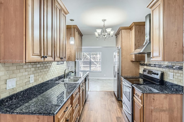 kitchen with sink, wall chimney exhaust hood, hanging light fixtures, appliances with stainless steel finishes, and light wood-type flooring