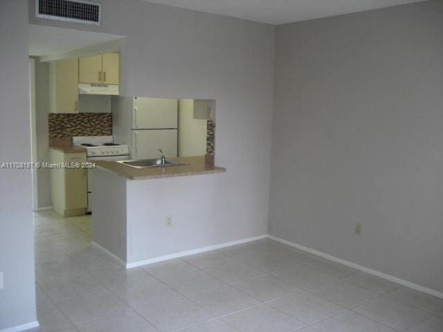 kitchen with kitchen peninsula, white appliances, sink, light tile patterned floors, and cream cabinetry