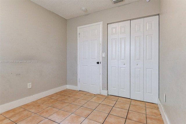 unfurnished bedroom featuring a textured ceiling, a closet, and light tile patterned flooring