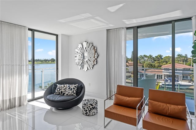 living area with tile patterned flooring, a water view, floor to ceiling windows, and a healthy amount of sunlight