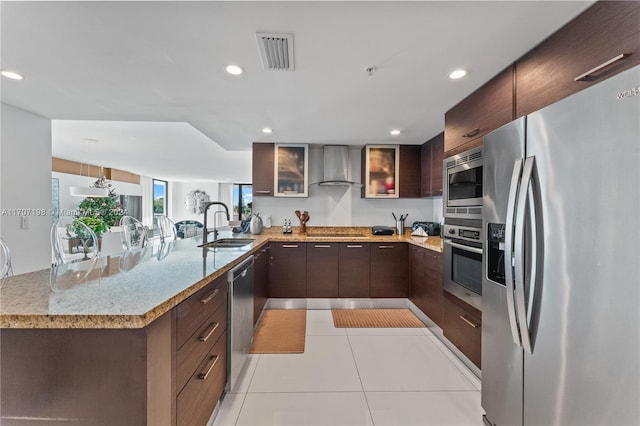 kitchen with kitchen peninsula, stainless steel appliances, sink, wall chimney range hood, and light tile patterned flooring