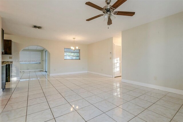 tiled empty room featuring ceiling fan with notable chandelier