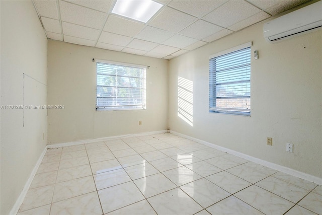 tiled empty room with a paneled ceiling, a healthy amount of sunlight, and a wall unit AC