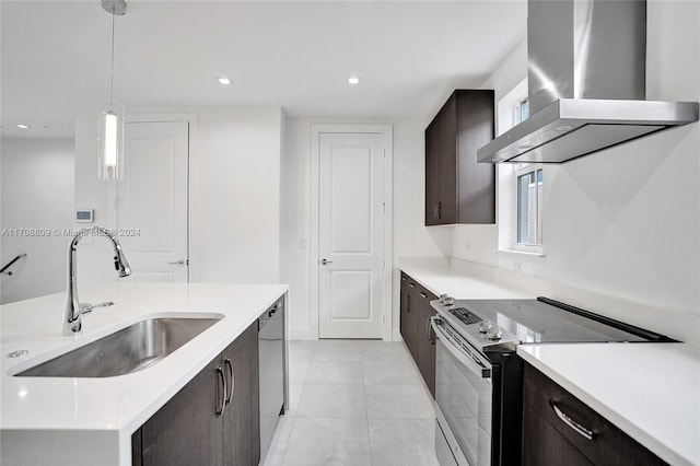 kitchen with wall chimney range hood, sink, light tile patterned floors, appliances with stainless steel finishes, and decorative light fixtures