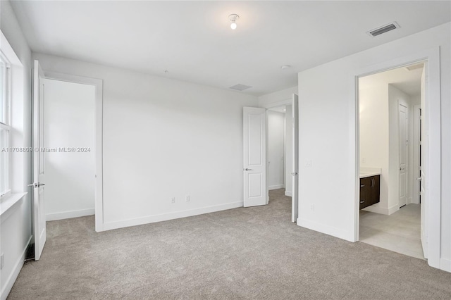 unfurnished bedroom featuring light carpet and ensuite bath