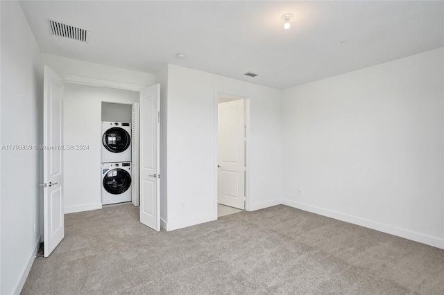 unfurnished bedroom with light colored carpet and stacked washer / drying machine