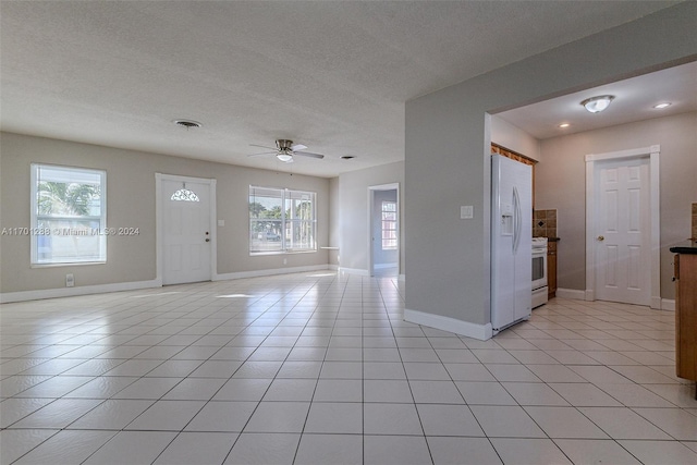 interior space featuring ceiling fan, light tile patterned flooring, a healthy amount of sunlight, and a textured ceiling