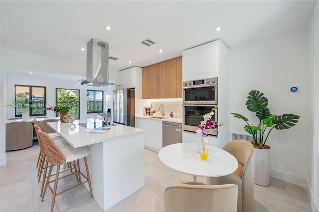 kitchen featuring island exhaust hood, a kitchen island, white cabinets, and appliances with stainless steel finishes