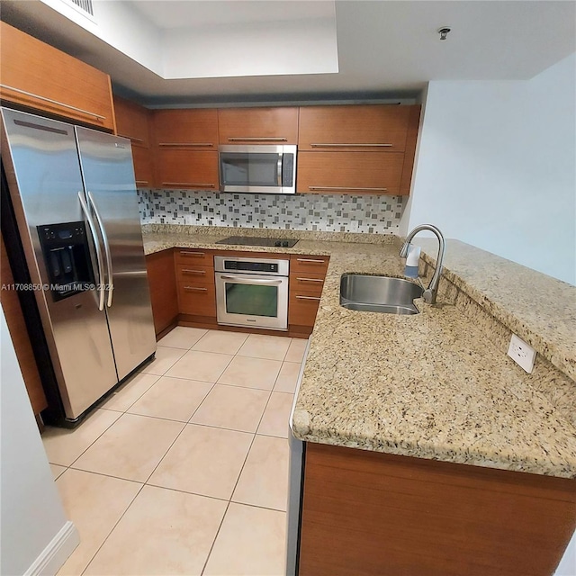 kitchen featuring sink, stainless steel appliances, light stone counters, kitchen peninsula, and decorative backsplash