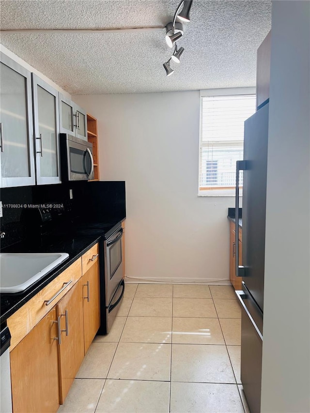 kitchen with a textured ceiling, light tile patterned floors, stainless steel appliances, and track lighting