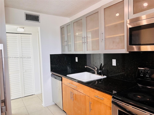 kitchen with appliances with stainless steel finishes, backsplash, a textured ceiling, sink, and light tile patterned flooring