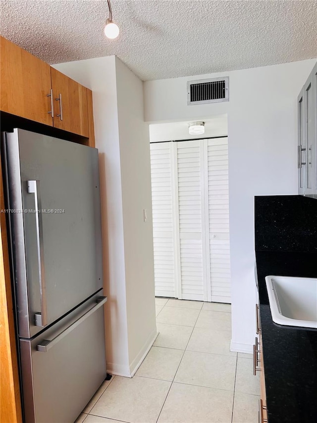 kitchen with sink, a textured ceiling, stainless steel refrigerator, and light tile patterned flooring