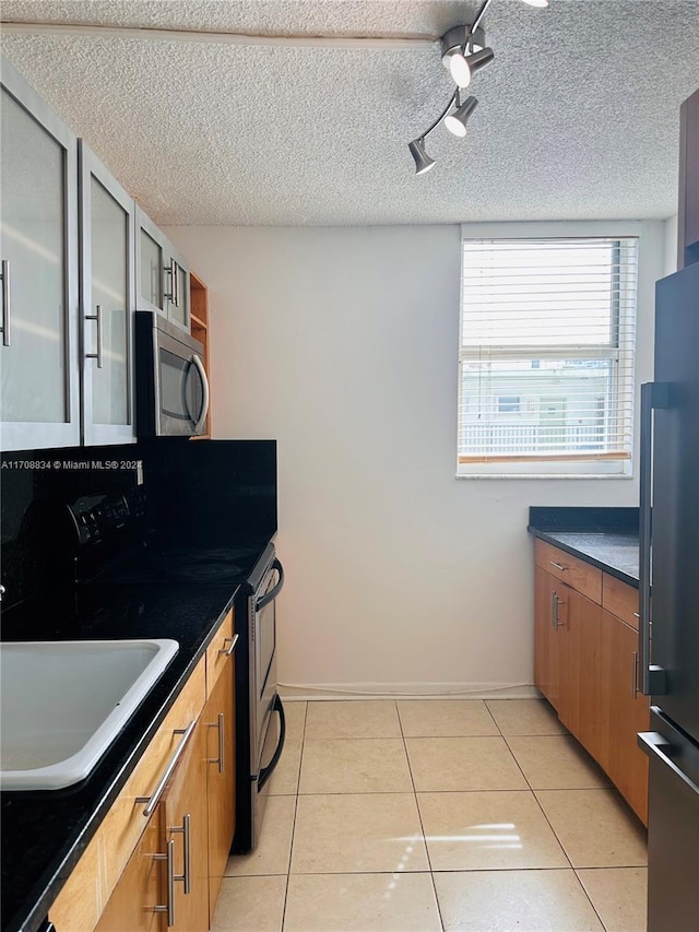 kitchen with appliances with stainless steel finishes, a textured ceiling, light tile patterned floors, and sink