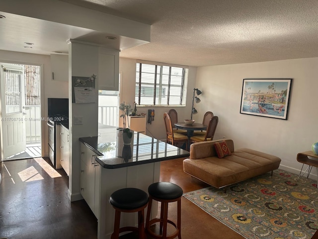 kitchen with kitchen peninsula, a breakfast bar, a textured ceiling, white cabinets, and stainless steel stove