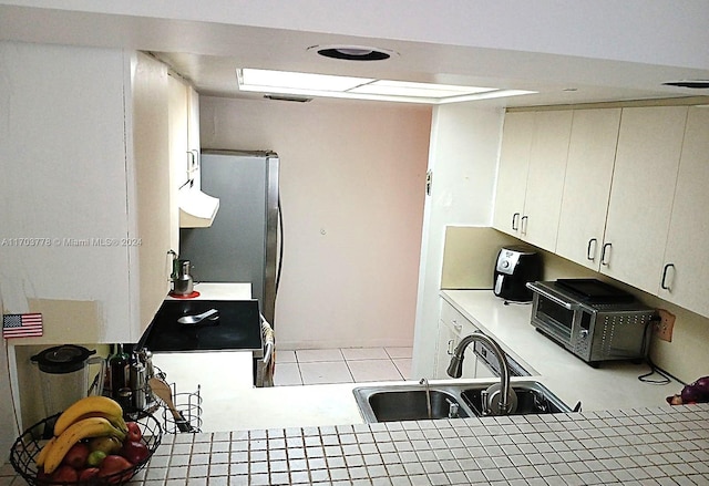 kitchen with white cabinetry, light tile patterned floors, sink, and stainless steel refrigerator