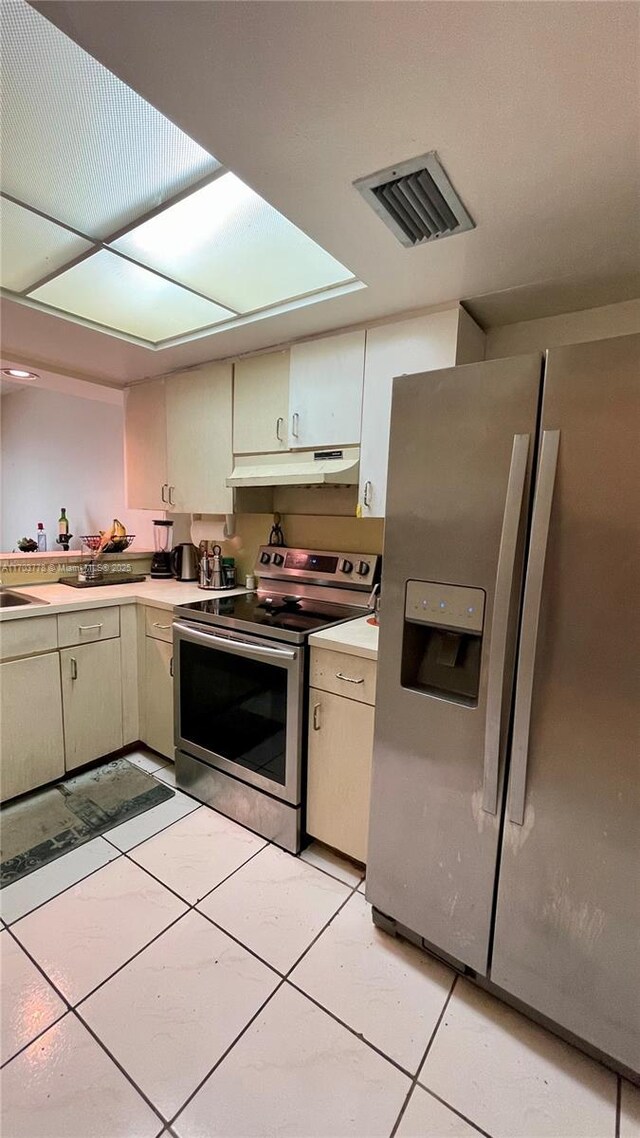 kitchen featuring cream cabinetry, appliances with stainless steel finishes, a skylight, and light tile patterned floors