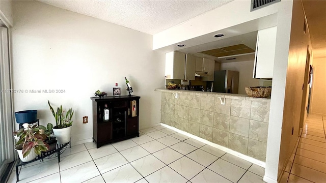 interior space featuring light tile patterned floors, a textured ceiling, white cabinetry, and stainless steel refrigerator