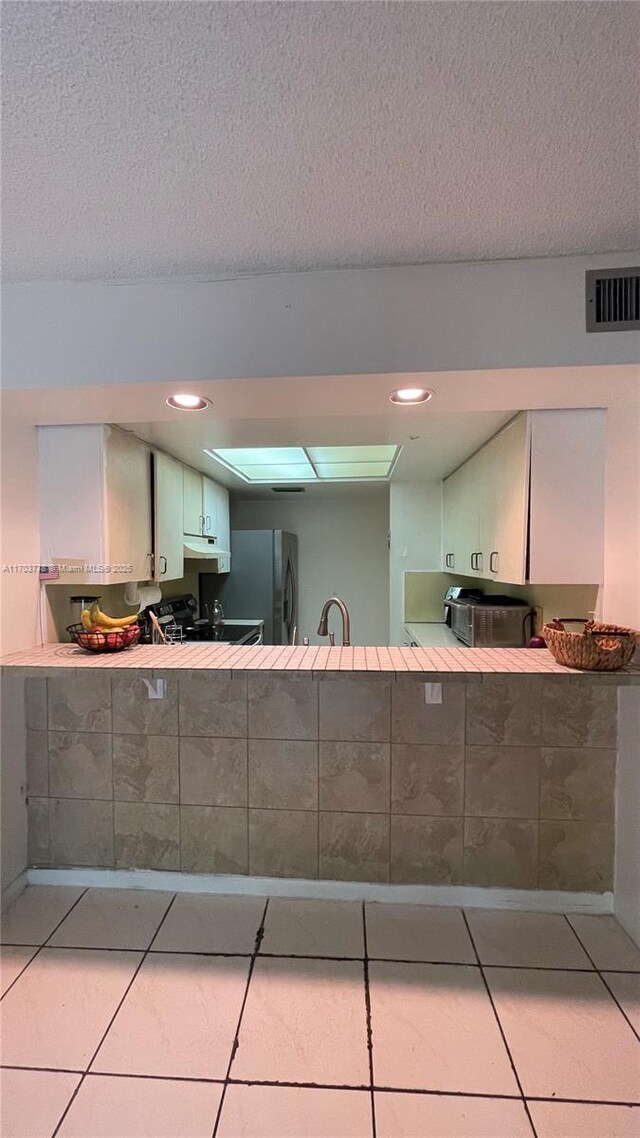 kitchen with stove, a textured ceiling, white cabinets, stainless steel refrigerator, and light tile patterned flooring