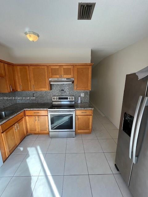 kitchen featuring decorative backsplash, light tile patterned floors, stainless steel appliances, and dark stone counters