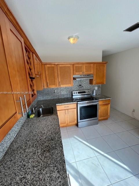 kitchen with stainless steel electric range oven, sink, tasteful backsplash, dark stone counters, and light tile patterned flooring