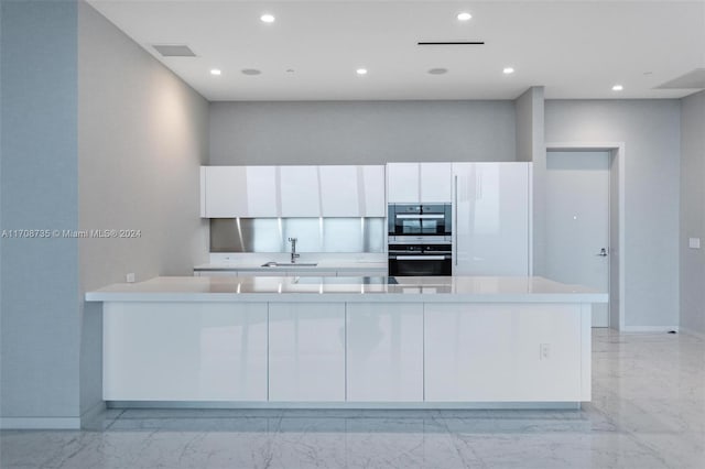 kitchen with kitchen peninsula, stainless steel double oven, white cabinetry, and sink