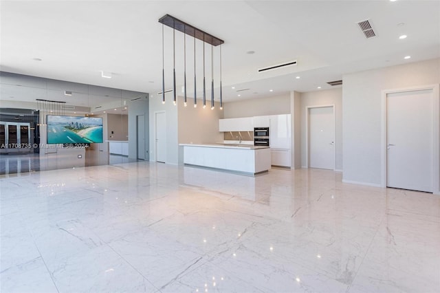 kitchen with stainless steel double oven, white cabinets, a spacious island, and decorative light fixtures