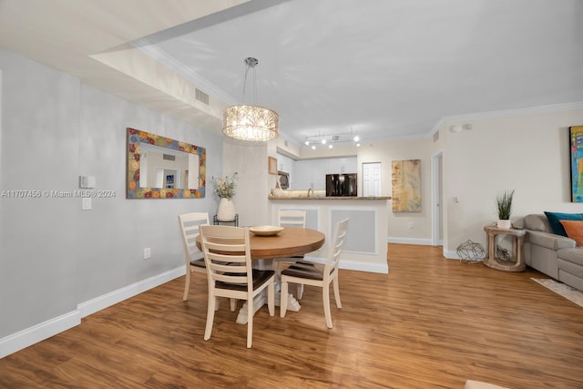 dining area with a notable chandelier, light wood-type flooring, ornamental molding, and track lighting