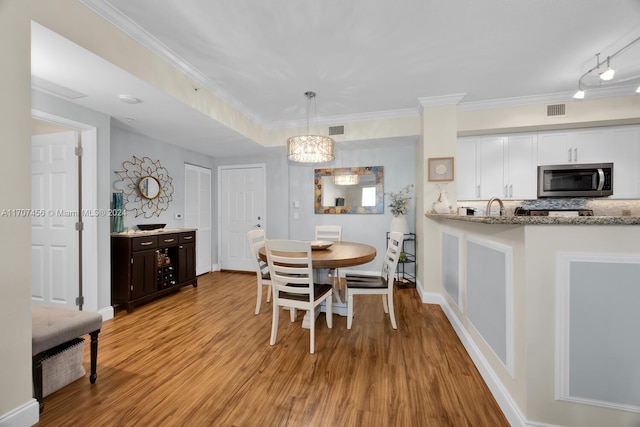 dining area featuring light hardwood / wood-style floors, sink, crown molding, and an inviting chandelier