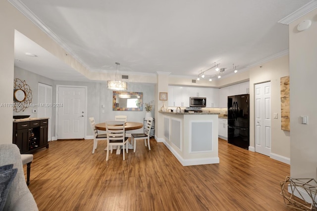 kitchen featuring white cabinets, black refrigerator, crown molding, hanging light fixtures, and light wood-type flooring