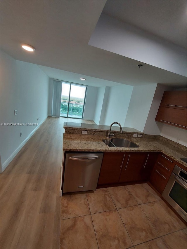 kitchen with sink, appliances with stainless steel finishes, light hardwood / wood-style floors, light stone counters, and kitchen peninsula