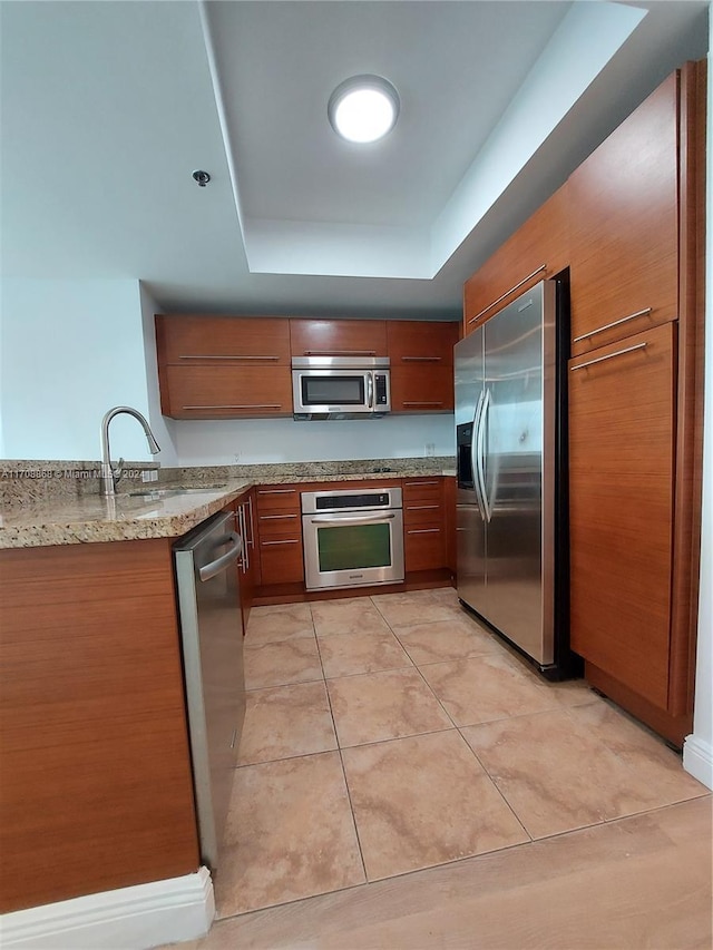 kitchen featuring light stone countertops, appliances with stainless steel finishes, a tray ceiling, sink, and light tile patterned flooring