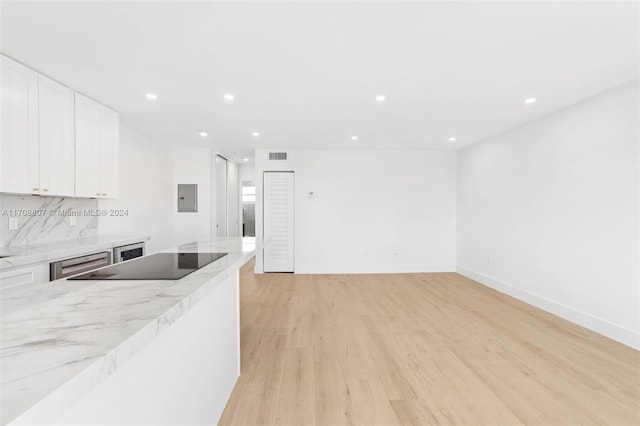 kitchen with light stone countertops, black electric stovetop, light hardwood / wood-style flooring, white cabinets, and electric panel