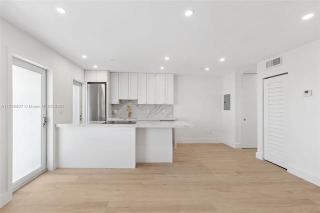 kitchen featuring tasteful backsplash, white cabinetry, stainless steel refrigerator, and light hardwood / wood-style flooring