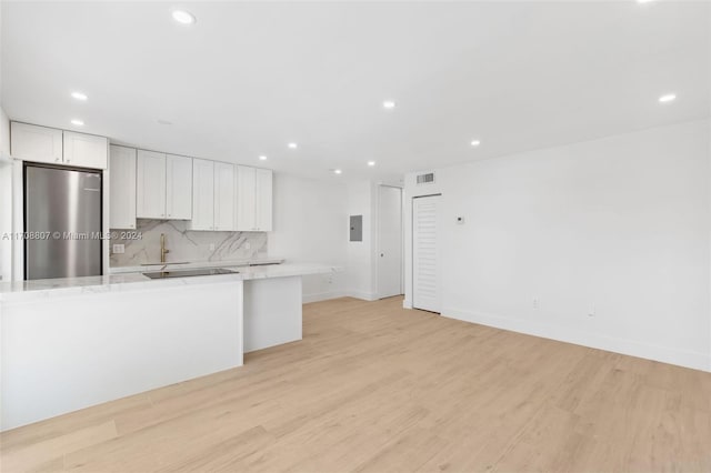 kitchen featuring light stone countertops, light wood-type flooring, tasteful backsplash, white cabinets, and stainless steel refrigerator