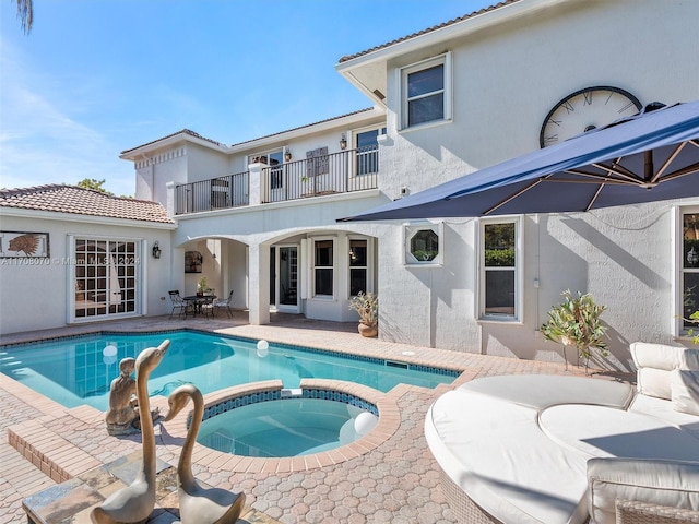 rear view of property with a pool with hot tub, a patio area, and a balcony