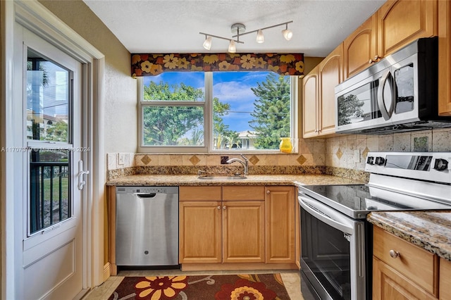 kitchen with appliances with stainless steel finishes, light stone counters, a healthy amount of sunlight, and sink