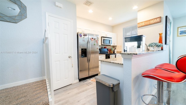 kitchen with kitchen peninsula, a kitchen breakfast bar, light stone countertops, stainless steel appliances, and white cabinets