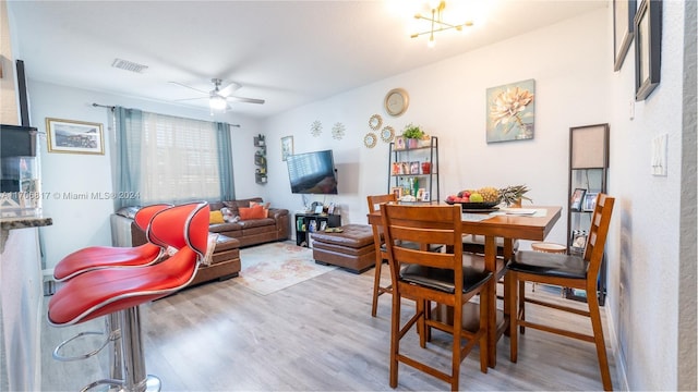 dining space with ceiling fan with notable chandelier and light wood-type flooring