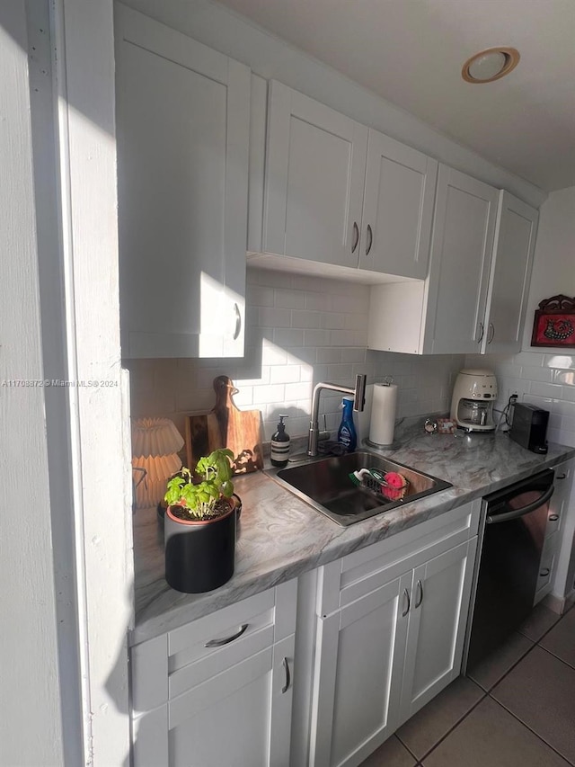 kitchen featuring tasteful backsplash, sink, light tile patterned floors, black dishwasher, and white cabinetry