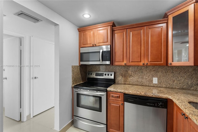 kitchen featuring backsplash, stainless steel appliances, light stone countertops, and light tile patterned floors