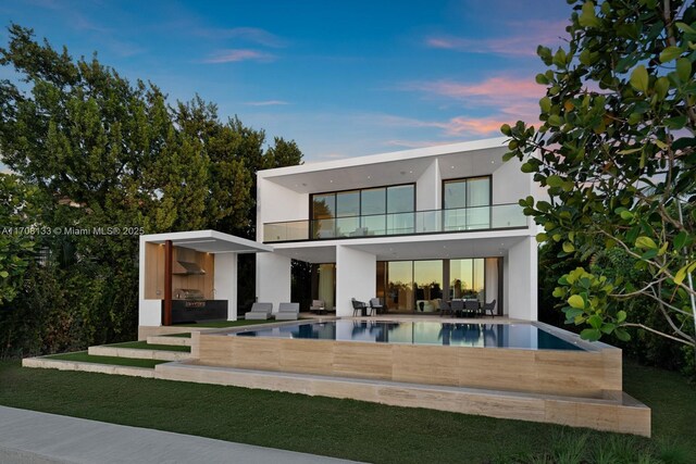 back house at dusk featuring outdoor lounge area, a balcony, and a patio area