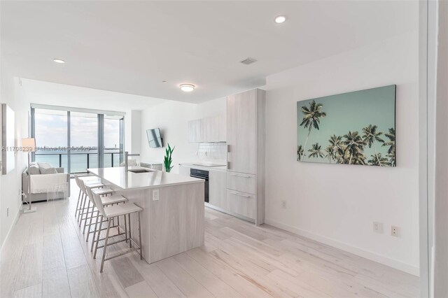 kitchen featuring light wood-type flooring, a kitchen island with sink, modern cabinets, and a kitchen bar