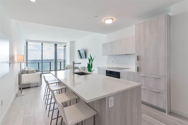 kitchen featuring an island with sink, modern cabinets, black appliances, a sink, and a breakfast bar area