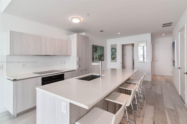 kitchen with modern cabinets, a sink, a breakfast bar, a kitchen island with sink, and black appliances