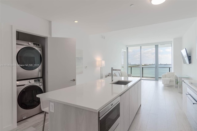 kitchen featuring white cabinetry, sink, expansive windows, stacked washer and dryer, and an island with sink